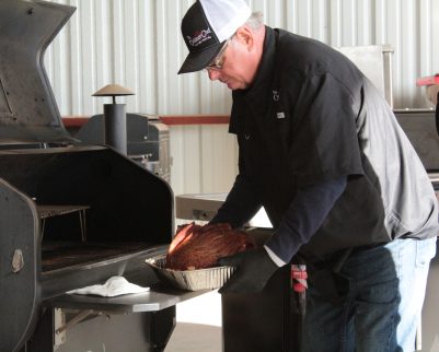 smoked ham being removed from a pellet grill